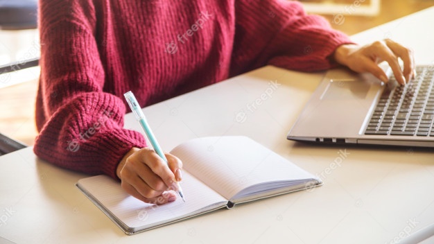 Девушка пишет в тетради и работает на своем ноутбуке на белом ...